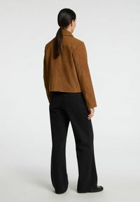 Brun ruskindsjakke med en skræddersyet pasform, cropped design og lange ærmer, parret med sorte vide jeans. Enkle og rene linjer.