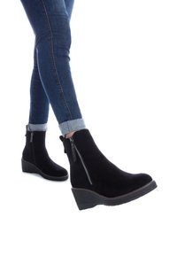 Botas de tobillo de ante negro con cuña y cremallera lateral. Las botas presentan una punta redondeada y una suela de goma texturizada para mayor agarre.