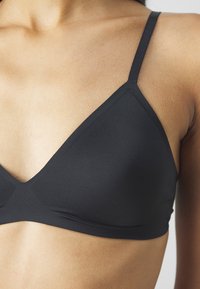 Black triangular bralette with narrow straps, smooth texture, and seamless design, featuring a deep V-neckline and minimalistic style.