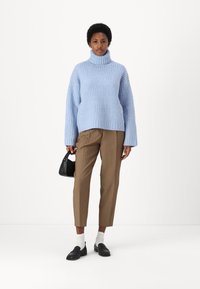 Ljusblå ribbad turtleneck-tröja, överdimensionerad passform, ihop med bruna skräddarsydda byxor och svarta loafers, håller en liten svart väska.