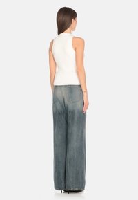 Top bianco aderente senza maniche abbinato a jeans a gamba larga di un blu chiaro, con un lavaggio sbiadito e orlo grezzo. Design semplice e moderno.