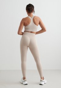 Conjunto deportivo beige con textura acanalada, que incluye un sujetador deportivo con diseño de tirantes cruzados en la espalda y leggings de talle medio. Combinado con zapatillas deportivas blancas.