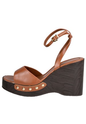 Sandalia cuña de cuero marrón con correa en el tobillo, hebilla dorada y tachuelas decorativas doradas en la suela plataforma texturizada de color marrón oscuro.