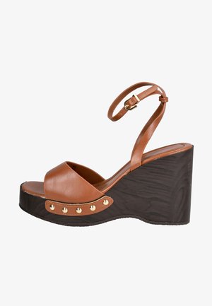 Sandalia cuña de cuero marrón con correa en el tobillo, hebilla dorada y tachuelas decorativas doradas en la suela plataforma texturizada de color marrón oscuro.