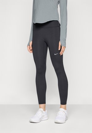 Leggings neri realizzati in tessuto elastico, con un design aderente e un piccolo logo bianco Nike sulla coscia sinistra. Indossati con una maglietta grigia e scarpe bianche.