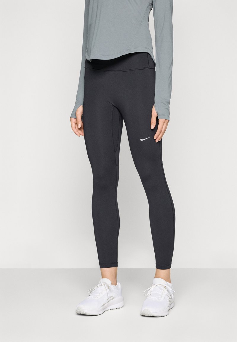 Leggings neri realizzati in tessuto elastico, con un design aderente e un piccolo logo bianco Nike sulla coscia sinistra. Indossati con una maglietta grigia e scarpe bianche.