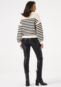 Chunky gebreide trui in crèmekleurige en zwarte strepen, met een hoge hals en ballonsleeves, gecombineerd met zwarte leren leggings en enkellaarsjes.