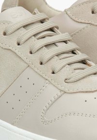 Světlé semišové a kožené tenisky s hladkým povrchem, kulatou špičkou, šesti tkanými tkaničkami a jemnými perforacemi na boku.