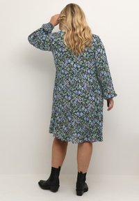 Vestido floral de mangas largas, con un fondo negro y patrones de flores en verde, azul y blanco. Combinado con botas negras hasta el tobillo.