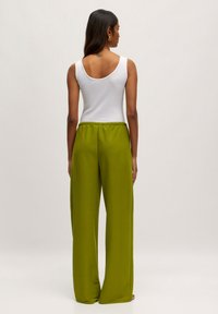Witte mouwloze top en hooggezakte, wijde groene broek van zacht materiaal. De broek heeft een elastische tailleband. Zichtbare tatoeage op de rug.