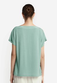 Mintgrünes Kurzarmoberteil mit lockerem Schnitt, glatter Textur und rundem Ausschnitt. Die Rückansicht zeigt eine klare Silhouette ohne Verzierungen.