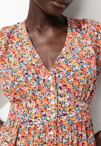Robe fleurie avec un décolleté en V, des manches courtes et une fermeture à boutons sur le devant. Le tissu est orné de nuances d'orange, de jaune et de bleu.