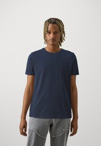 Sötétkék pamut póló kerek nyakkivágással és rövid ujjakkal. Puha tapintású, slim fit fazonú, világosszürke nadrággal párosítva, ami nappali zsebekkel van ellátva.