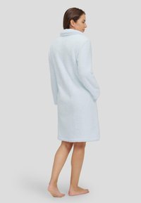 Bata de baño de color azul claro y esponjosa, con cuello chal, mangas largas y bolsillos laterales. Diseño hasta la rodilla con una tela suave y texturizada.