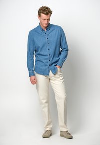 Lichtblauw denim overhemd met knopen en lange mouwen, gecombineerd met beige broeken en lichte schoenen; heeft een klassieke kraag en frontzakken.