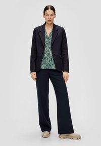 Marineblazer met één knop, groen patroon blouse, wijdvallende marineblauwe broek en lichtbeige platform schoenen. Glad stoftexturen.