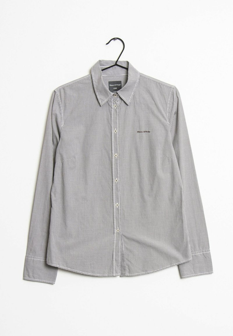 Chemise à manches longues avec petit motif à carreaux suspendue sur un cintre noir sur fond blanc.