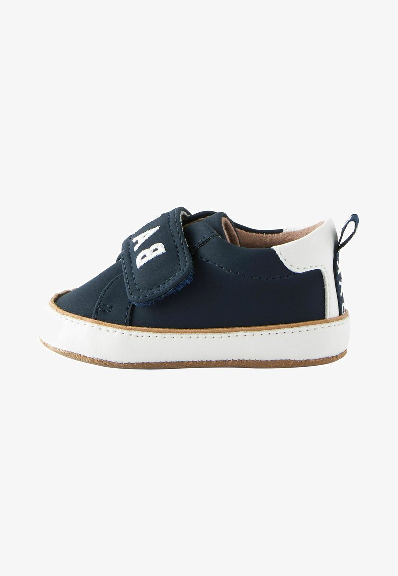 Marineblaue Stoffschuhe mit weißen Akzenten, ausgestattet mit einem Klettverschluss und einer abgerundeten Spitze. Gummisohle mit hellbraunen Akzenten und einer kleinen Lasche auf der Rückseite.