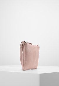 Růžová kožená kabelka s hladkým povrchem, čtvercovým tvarem, bočním zipem a krátkým popruhem, vystavená pod mírným úhlem.