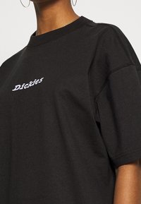 Svart bomullströja med rund halsringning, oversized passform och broderad "Dickies"-logotyp i vitt på bröstet. Synlig sömnadsdetalj.
