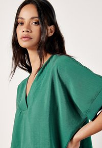 Top verde a maniche corte con scollo a V e vestibilità morbida. Realizzato in tessuto testurizzato, presenta pieghe sottili e una silhouette rilassata.