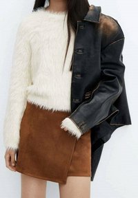 Czarny skórzany płaszcz o postarzanym wykończeniu, biały puszysty sweter i brązowa zamszowa mini spódniczka. Miękkie tekstury i kontrastujące kolory.