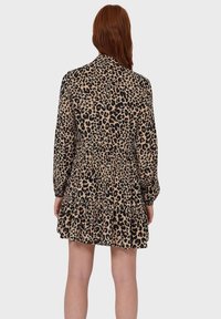 Sukienka w panterkę z długimi rękawami, marszczoną talią i warstwową spódnicą. Wykonana z lekkiego materiału w odcieniach beżu, czerni i brązu.