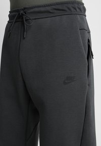 Mörkgrå bomullssvetter med elastisk midja och dragsnören, sidofickor med dragkedja och en subtil svart Nike-logotyp på låret.