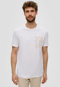 Biała bawełniana koszulka z krótkim rękawem, z beżową kieszonką w wzory po lewej stronie oraz okrągłym dekoltem. Minimalistyczny design.