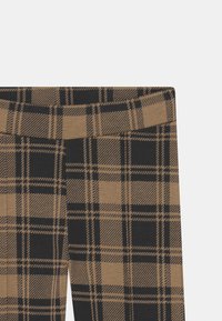 Hnědé a černé kostkované legíny s hladkým povrchem, s širokým elastickým pasem a výrazným kostkovaným vzorem.