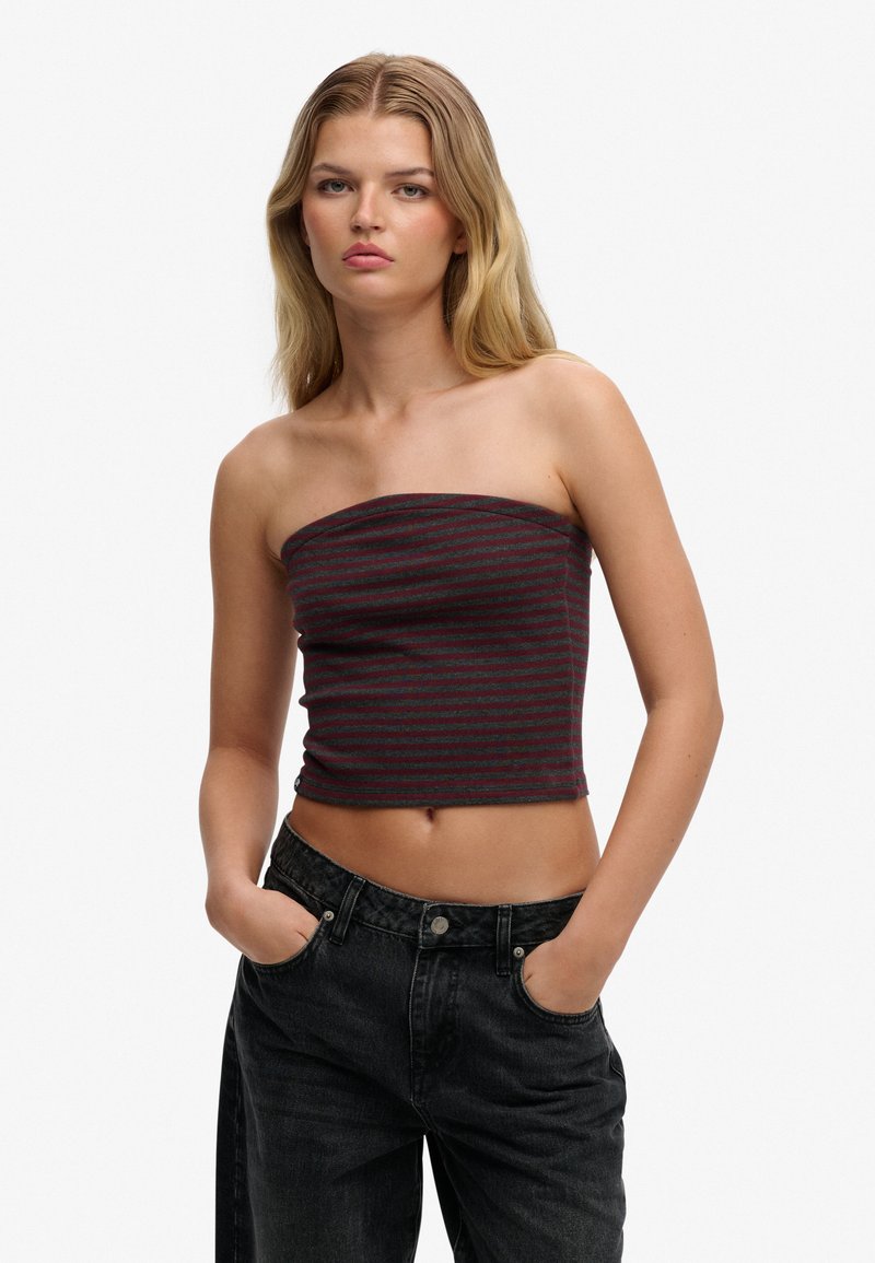 Top corto sin tirantes en gris oscuro con rayas rojas. Tejido suave, diseño ajustado, combinado con jeans negros de talle alto.