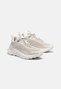 Zapatillas ligeras con una parte superior de malla transpirable en beige, detalles texturizados y una entresuela blanca salpicada. Diseñadas para ofrecer tracción.