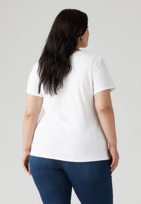 Camiseta de algodón blanca con un cuello redondo clásico, mangas cortas y un corte recto, combinada con jeans de mezclilla azul. La vista trasera muestra una textura suave.