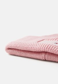 Écharpe en tricot rose avec une texture en côtes, pliée soigneusement. Présente un petit écusson logo aux couleurs contrastées sur la surface.