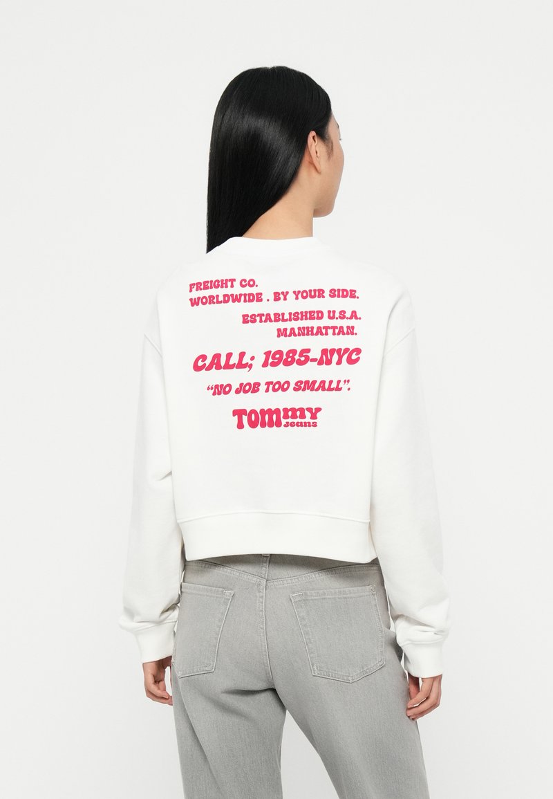 Witte cropped sweatshirt met rode grafische tekst op de achterkant. De tekst omvat de merknaam en de vestigingslocatie. De stof is soepel en heeft een casual pasvorm.
