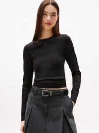 Svart langermet topp med teksturert stoff, med en liten logodetalj. Kombinert med et grått skjørt og svart belte med metallspenne.