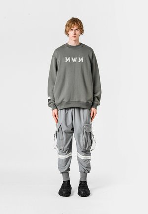 Sudadera gris con letras "MWM", combinada con pantalones cargo grises que tienen bolsillos laterales y acentos en blanco contrastantes. Footwear negro completa el look.