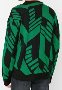 Pull en maille noir et vert avec un motif géométrique. Coupe ample, manches longues et col rond. Tissu texturé.