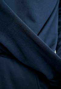 Tmavomodrá flísová látka s hladkou textúrou, obsahujúca záhyby a prekrývajúci sa dizajn, predstavujúca mäkký, teplý materiál.