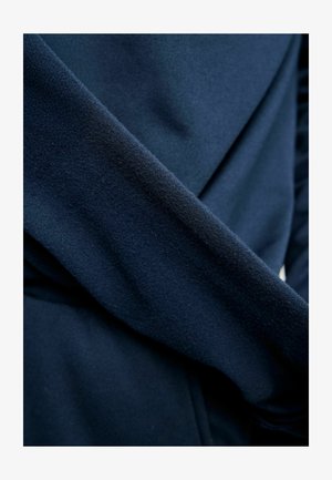 Marineblauwe fleece stof met een gladde textuur, voorzien van gedrapeerde delen en een overlappend ontwerp, die zacht en warm materiaal toont.