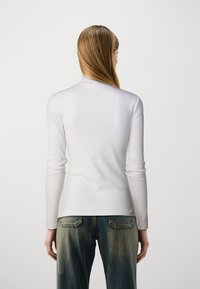 Vit långärmad ribbad topp med en kroppsnära design, som har hög halsringning och mjuk textur, kombinerad med urtvättade blåjeans.