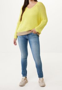 Yellow knitted sweater with a beige hem, paired with light blue skinny jeans and beige sneakers. The sweater features a wide neckline and loose fit.