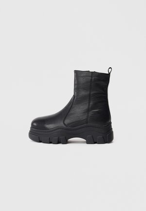 Bottines noires en cuir lisse avec une semelle en caoutchouc épaisse, dotées d'une fermeture éclair latérale et d'une languette à l'arrière pour un enfilage facile.