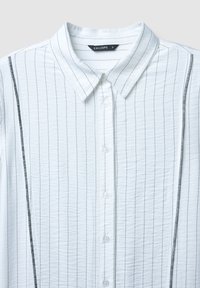 Camicia bianca con bottoni a lungo, strisce nere verticali, tessuto testurizzato, colletto e cinque bottoni sul davanti. Etichetta del marchio: Calliope.