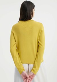 Gelbes gestricktes Sweatshirt mit langen Ärmeln, gerippter Textur und runder Ausschnitt. Der Rücken hat einen geraden Schnitt und subtile Nahtdetails.
