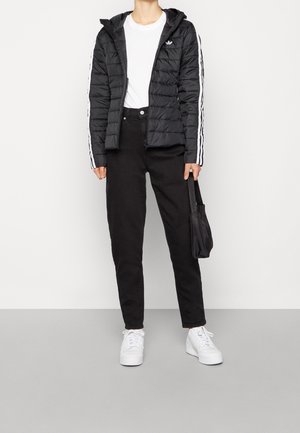 Černá prošívaná bunda s kapucí, se bílými pruhy na rukávech, nošená přes bílé tričko a kombinovaná s černými kalhotami a bílými teniskami.