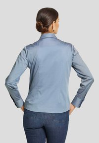 Himmelblaues Hemd mit Kragen und langen Ärmeln, glatte Textur, Ein-Knopf-Manschetten und taillierte Passform, kombiniert mit dunklen Denim-Jeans.