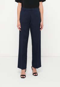 Námořnické široké kalhoty s hladkým povrchem, strukturovaným pasem a bočními kapsami, doplněné černými sandály na podpatku.