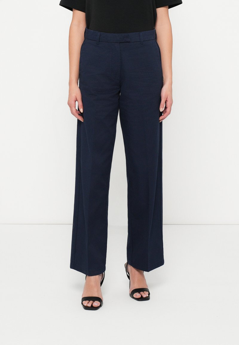 Námořnické široké kalhoty s hladkým povrchem, strukturovaným pasem a bočními kapsami, doplněné černými sandály na podpatku.