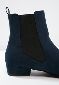 Botte Chelsea en daim bleu marine avec panneau latéral élastique noir, petit talon carré et languette à l'arrière.